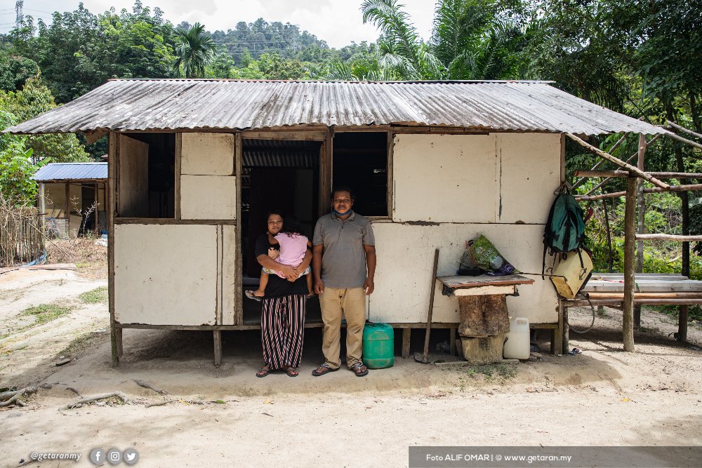 Haniza Rimba dan suami, Jon Kasni, berdiri di hadapan rumah mereka yang serba kekurangan di kampung Bukit Galah. 