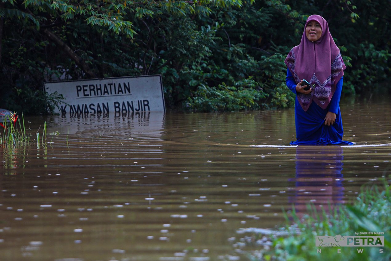 Seorang wanita meredah banjir berhampiran papan tanda mengenai amaran banjir di Meru, Klang, baru-baru ini. - Gambar oleh Sairien Nafis
