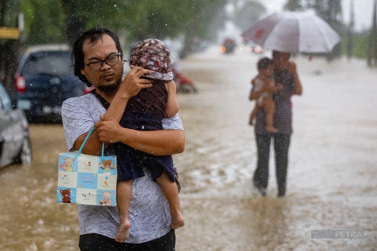 Seorang bapa meredah hujan sambil mendukung anaknya di kawasan Meru, Klang.