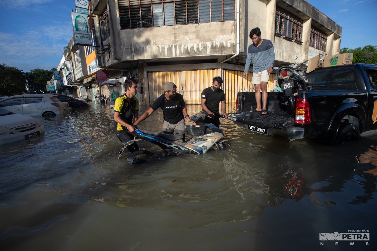 Beberapa pemuda cuba menaikkan sebuah motosikal yang terendam di dalam air banjir sejak Sabtu lalu, untuk dibawa ke bengkel.