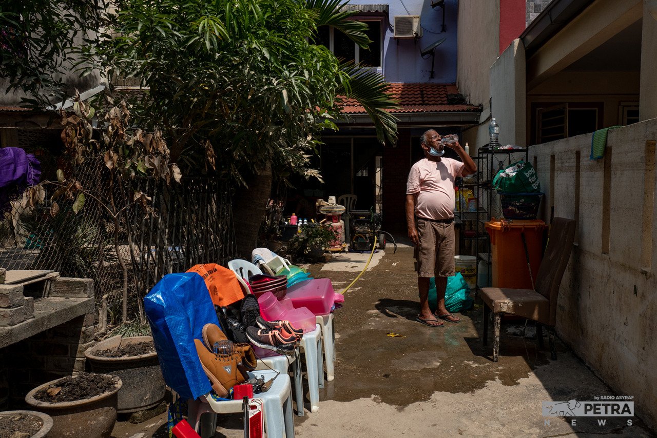 Ernest Alam Jansz meneguk air bagi menghilangkan dahaga selepas penat mencuci dan mengemas rumahnya yang ditenggelami air di Taman Sri Muda, Shah Alam. - Gambar Sadiq Asyraf