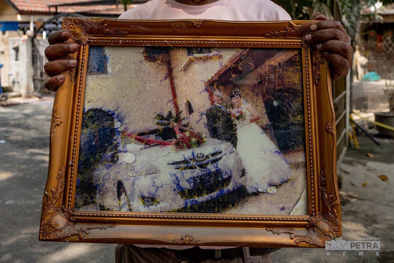 Ernest Alam Jansz menunjukkan potret perkahwinannya yang rosak selepas terkena banjir. - Gambar Sadiq Asyraf