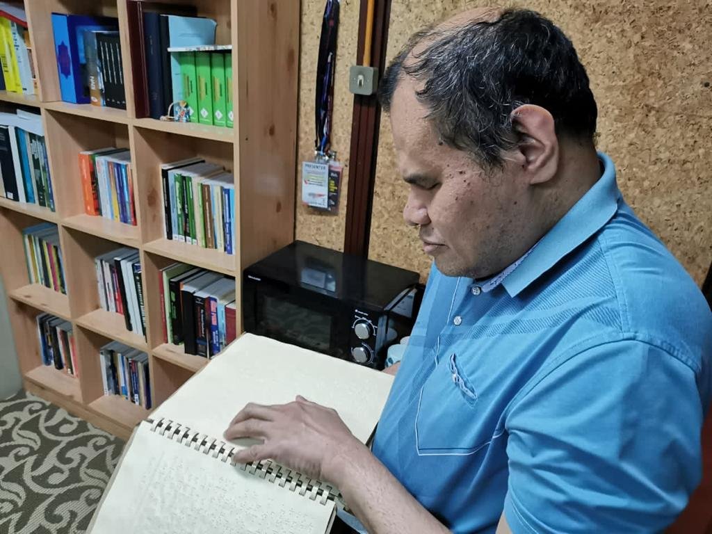 Dr Al-Amril sedang membaca buku menggunakan kaedah Braille ketika ditemui di UKM, baru-baru ini.