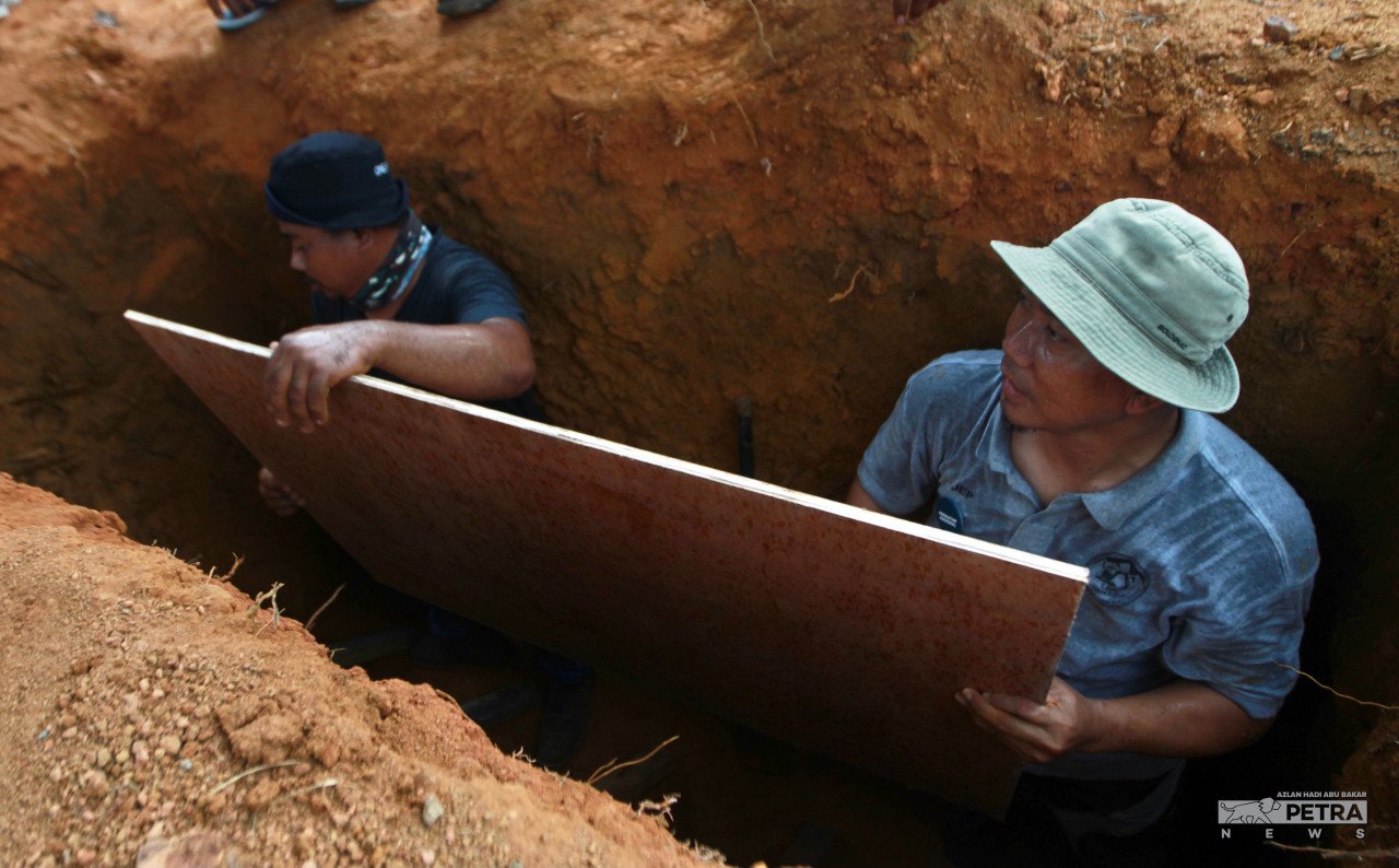 Jefri dan rakannya sedang menyiapkan liang lahad sebelum jenazah dikebumikan. gambar Azlan Hadi Abu Bakar