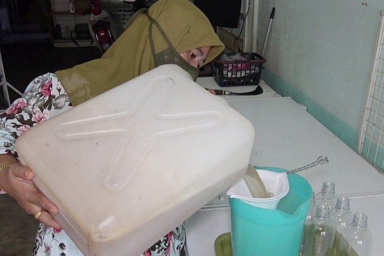 Sanisah Mohamed sedang mengisi air nira kelapa ke dalam botol sebelum disimpan dalam peti sejuk beku.