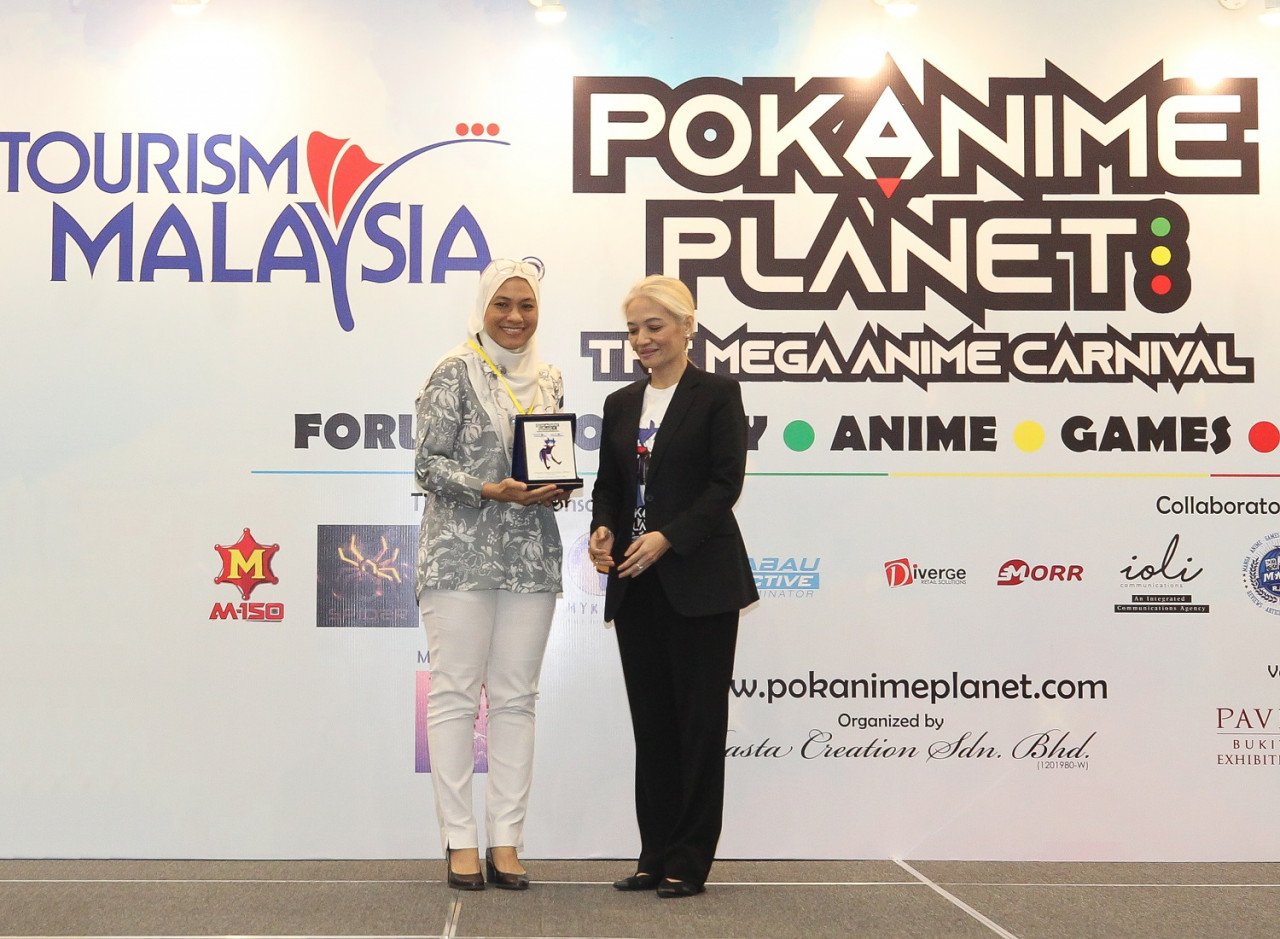 Pengerusi Pokanime Planet dan Pengasas Rasta Creations Sdn Bhd, Rasta Rashid menyerahkan cenderamata penghargaan kepada Timbalan Pengarah Tourism Malaysia, Nor Aida Ismail sebagai tanda kolaborasi antara Pokanime Planet bersama Tourism Malaysia.