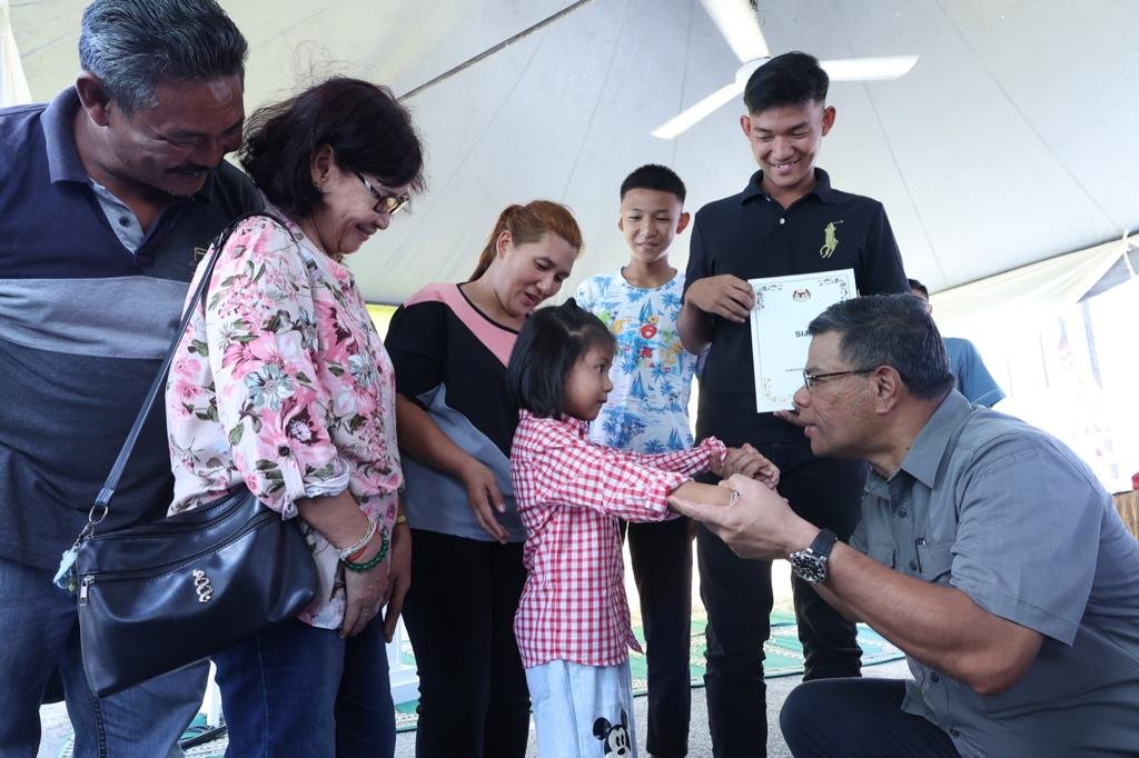 Menteri Dalam Negeri, Datuk Seri Saifuddin Nasution Ismail melayani telatah seorang daripada adik Khatanak selepas menyerahkan surat kelulusan permohonan kewarganegaraan remaja itu, hari ini. – gambar Rafisqi Radhi