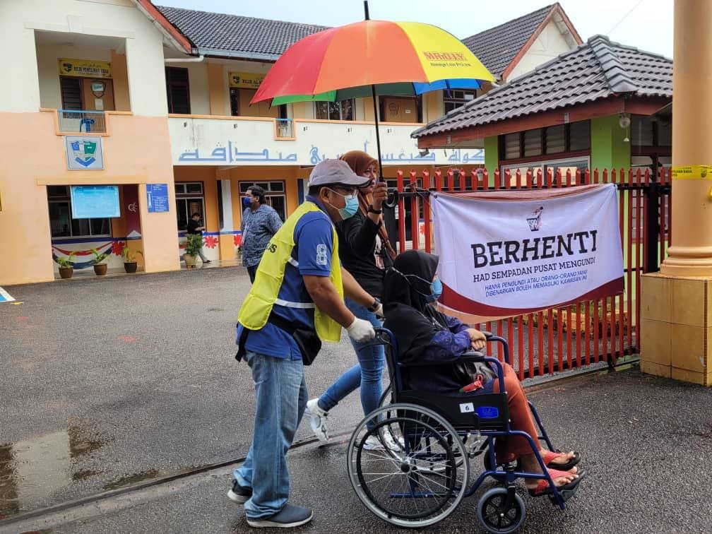 Petugas PRU-15 membantu pengundi kurang upaya di sebuah pusat mengundi di Parlimen Jasin, Melaka. - Gambar oleh P Kirtigha