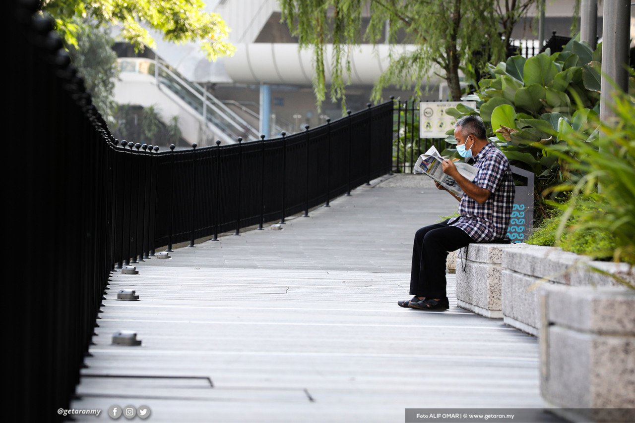 Seorang lelaki membaca akhbar dalam keadaan tenang, sendirian tanpa gangguan.
