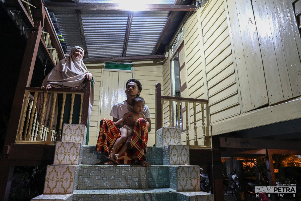 Noraini Ahmad Supan bersama anaknya, Muhammad Rezqy Adli Syam Tabri berehat di tangga rumah sambil menunggu ketibaan ahli keluarga yang lain.