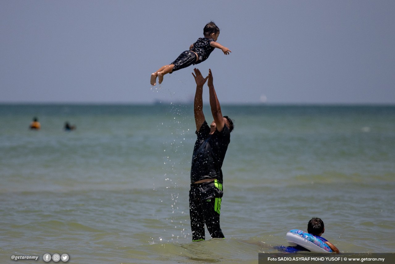Seorang bapa melambung anaknya ketika bermain air di Pantai Saujana, Port Dickson.
