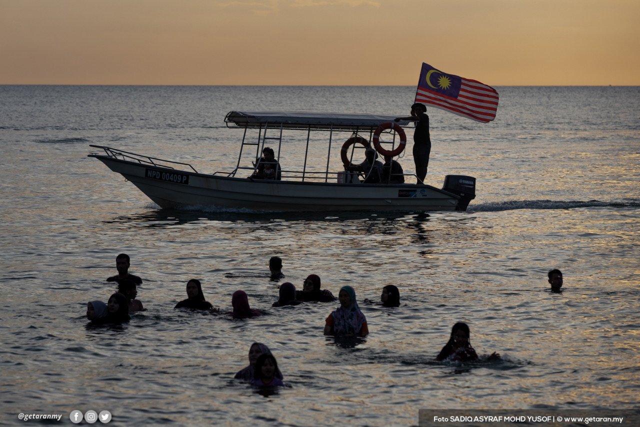 Gambar 'silhouette' pengunjung yang sedang bermandi-manda di Pantai Teluk Kemang, Port Dickson.