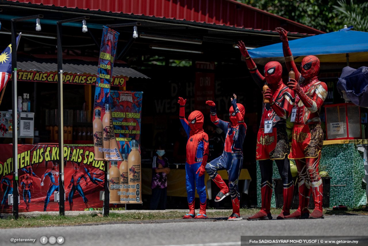 Penjual air sekeluarga memakai kostum Spiderman menjaja teh ais kepada pelancong. - Gambar oleh Sadiq Asyraf 