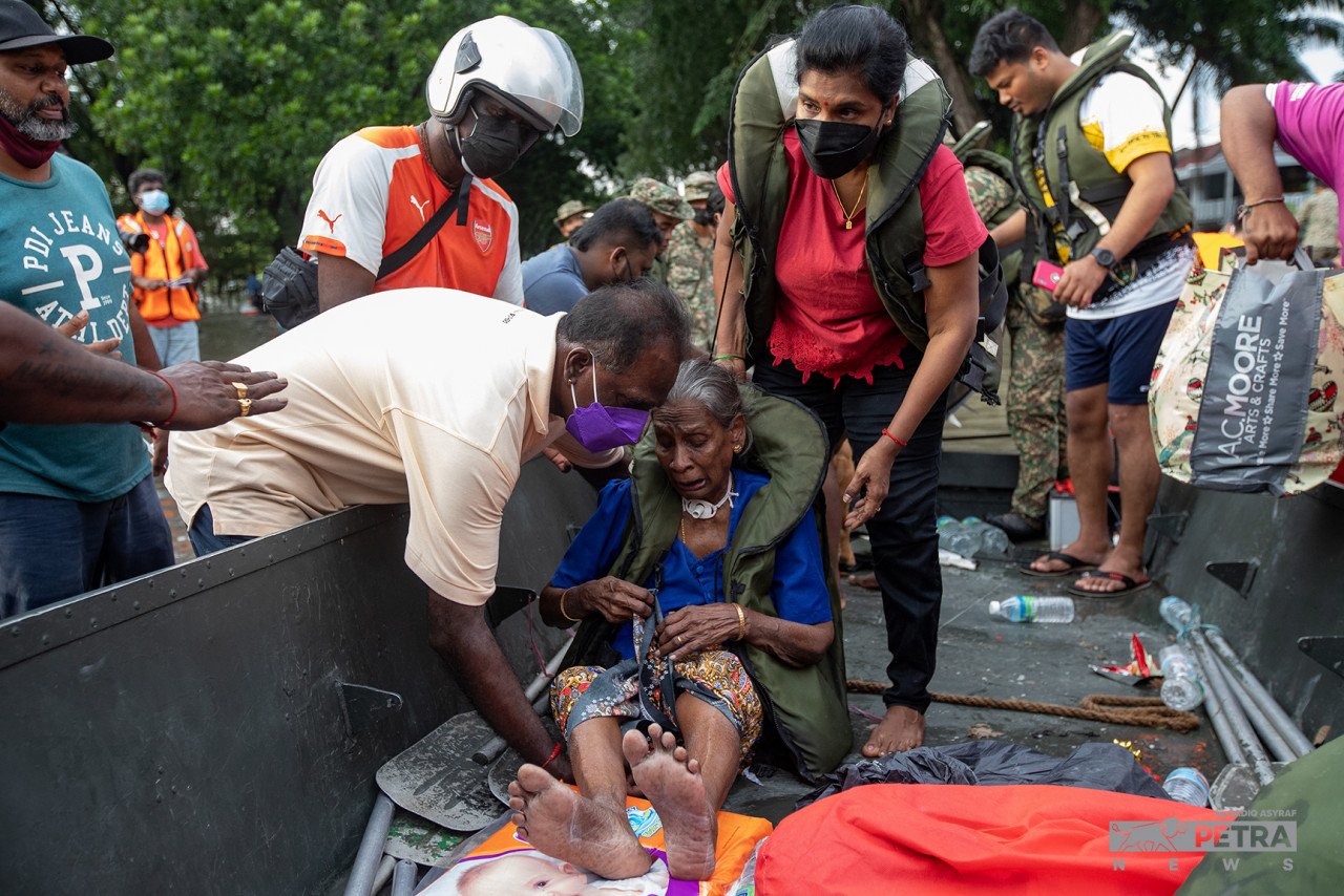 Orang ramai membantu memindahkan seorang warga emas yang terlibat dalam banjir di Taman Sri Muda, Shah Alam ke tempat selamat, pada Disember 2021. - Gambar fail