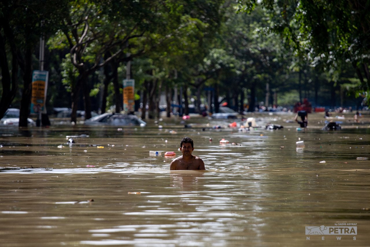 Seorang lelaki mengharungi air banjir atau fenomena air termenung, di Taman Sri Muda, Seksyen 25, Shah Alam, hari ini. 
