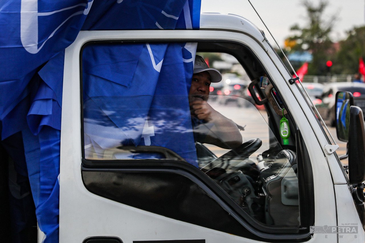 Seorang pemandu lori yang juga petugas jentera BN membawa bendera untuk dipacak di sekitar kawasan DUN Johor Jaya.