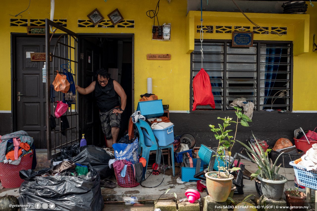 Salah seorang penduduk di Kampung Kebun Bunga membersihkan rumahnya selepas dilanda banjir kilat.