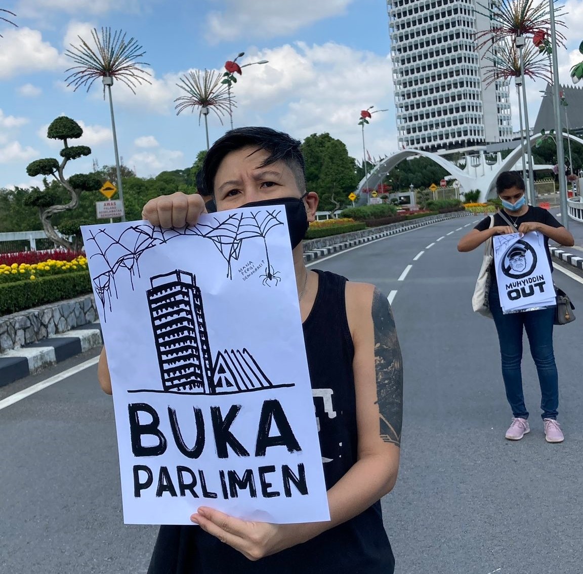 Seorang penunjuk perasaan memegang sepanduk tertera mesej menggesa supaya Parlimen dibuka. - Gambar dari Twitter Fahmi Reza