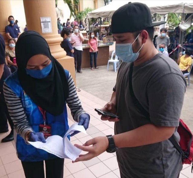 Seorang sukarelawan PPV Wisma Belia Indera Mahkota sedang membantu penerima vaksin menyemak pendaftaran mereka.